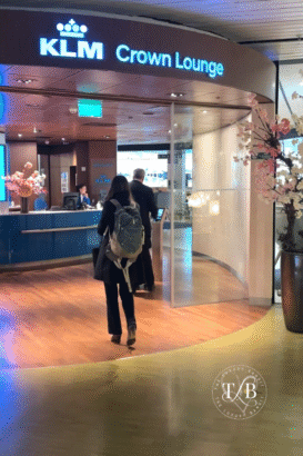 Traveler entering KLM Crown Lounge at Amsterdam Airport, greeted by modern decor and welcoming staff—an upscale travel lounge offering premium amenities for international passengers seeking comfort and convenience before long-haul flights.