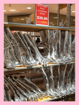 A rack of shiny silver boots at a Dillard's Clearance Center, with a "New Lower Price Clearance Shoes" sign. This highlights amazing discount designer shoes and incredible Dillard's sale tips for luxe for less shopping.