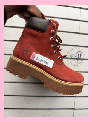 A hand holding up a pair of red Timberland boots with a price tag, showcasing Timberland boots on sale at a Dillard's Clearance Center. A great example of finding designer clothes for less.