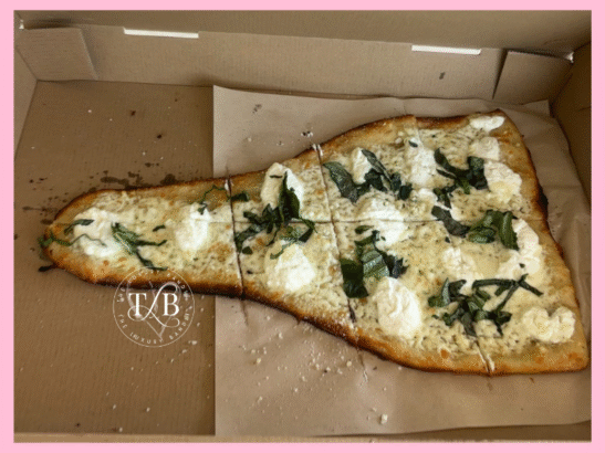 An irregularly shaped white pizza with dollops of ricotta and basil in a pizza box, with The Luxury Bandit logo. This visually showcases the Italian rustica pizza and unique pizza shapes that make for a memorable Crust Pizzeria Tempe review.