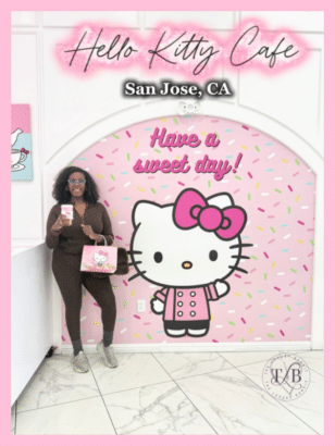 Woman in sunglasses holding Hello Kitty drink and bag poses at Hello Kitty Cafe San Jose entrance, featuring large pink donut wall with kawaii Hello Kitty character and "Have a sweet day" message